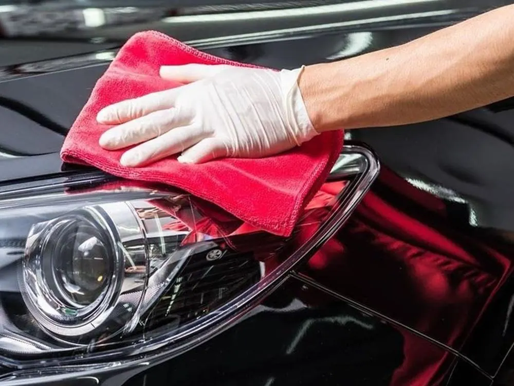 Technician hand-finishing a vehicle headlight and fender