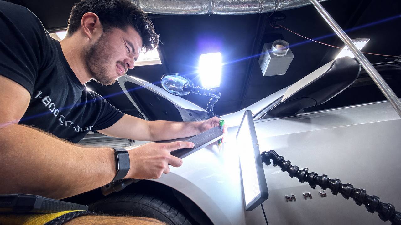 1-800-DENT-DOC technician reading a dent with an LED light board during paintless dent repair on a silver vehicle