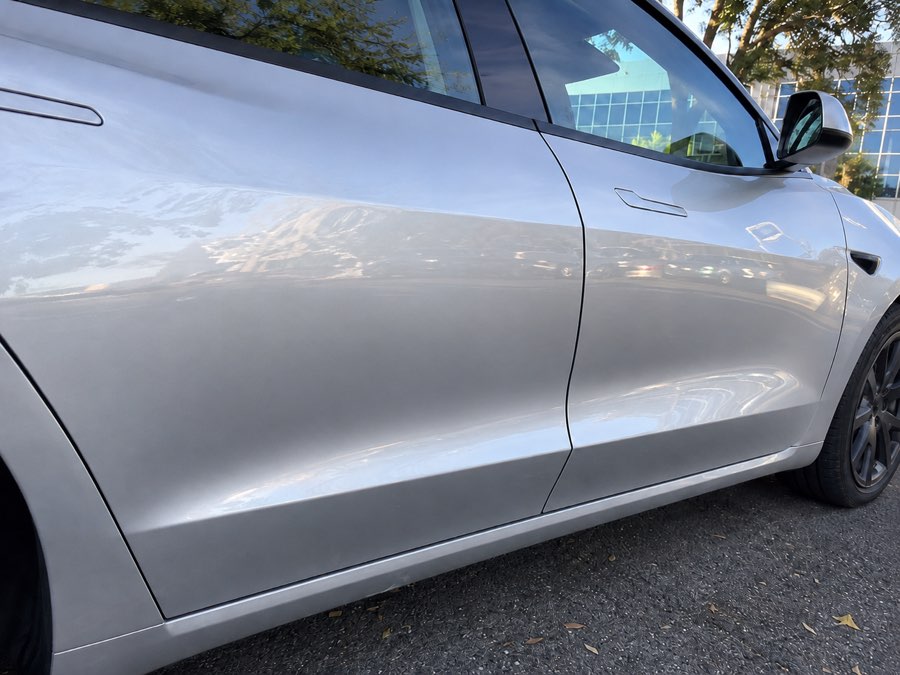 The same silver Tesla door panel after paintless dent repair, with the dent fully removed